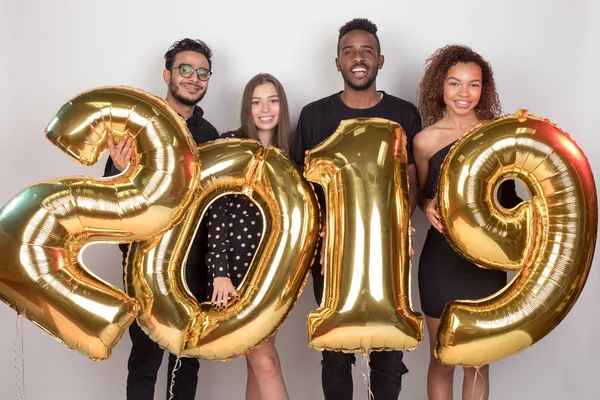 Joven compañía de amigos sosteniendo cartel 2019 hecho de globos de oro para el nuevo año sobre fondo blanco . — Foto de Stock