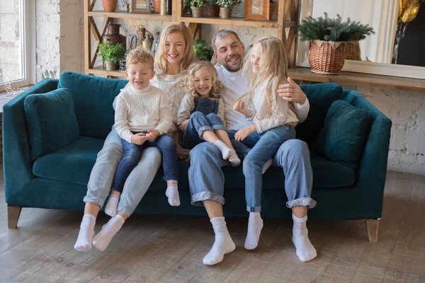 Padres felices y niños divirtiéndose haciendo cosquillas sentados juntos en el sofá . — Foto de Stock