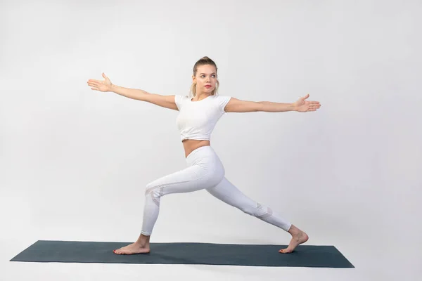 Spor yapan genç bir kadın beyaz arka planda yoga yapıyor..