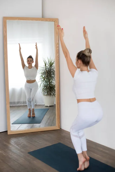 Mujer joven deportiva haciendo yoga frente al espejo en casa . — Foto de Stock