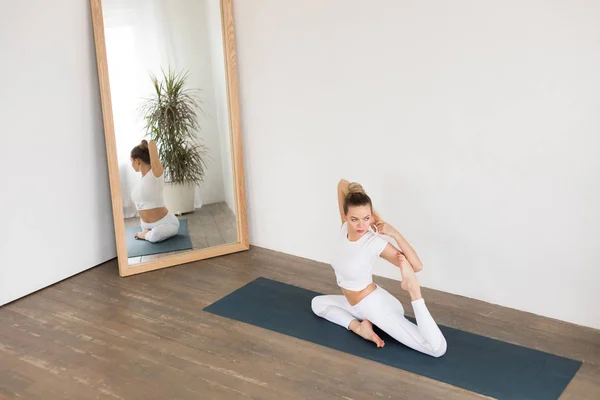Mujer joven deportiva haciendo yoga frente al espejo en casa . — Foto de Stock