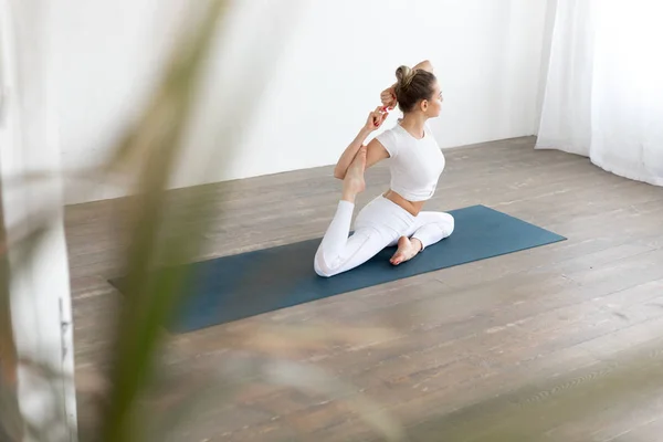 Mujer joven deportiva haciendo práctica de yoga sobre fondo blanco en casa . — Foto de Stock