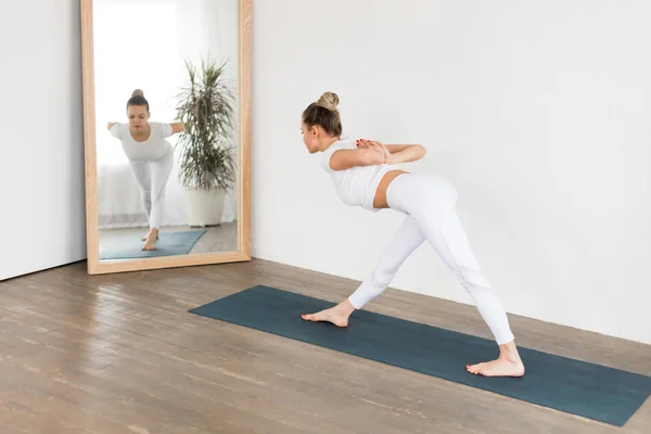 Sportieve jonge vrouw doen yoga praktijk op witte achtergrond thuis. — Stockfoto