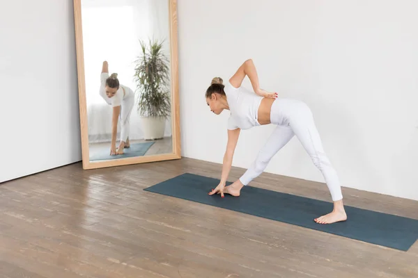 Mujer joven deportiva haciendo práctica de yoga sobre fondo blanco en casa . — Foto de Stock