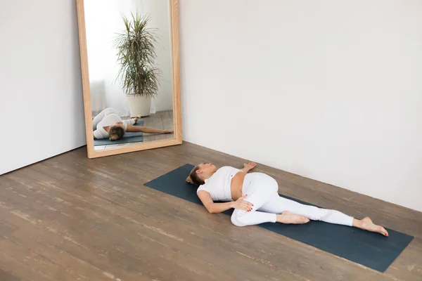 Mujer joven deportiva haciendo práctica de yoga sobre fondo blanco en casa . — Foto de Stock