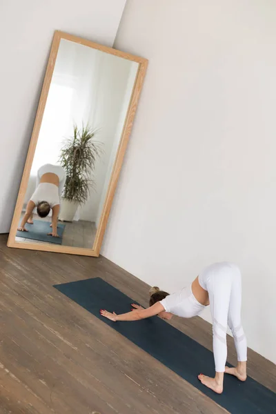 Mujer joven deportiva haciendo práctica de yoga sobre fondo blanco en casa . — Foto de Stock