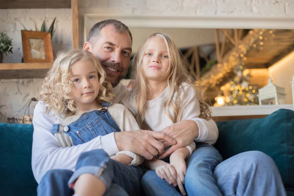 Far sitter med sina två döttrar på soffan hemma. — Stockfoto