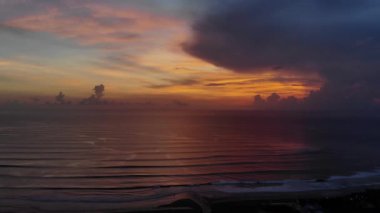 Günbatımı sırasında bulutlu gökyüzüne karşı okyanusun pastoral drone görüntüleri.