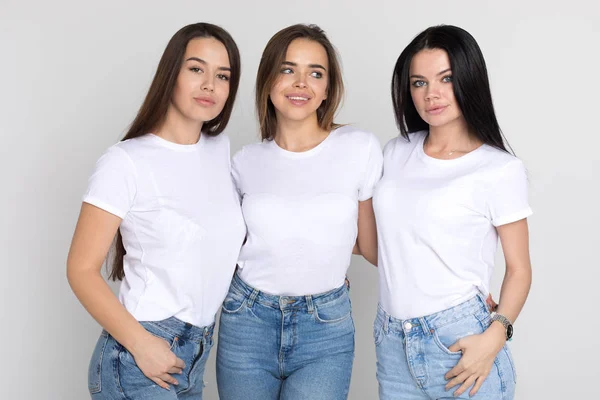 Tres hermosas y divertidas mujeres jóvenes en camisetas blancas y jeans sobre un fondo blanco . — Foto de Stock