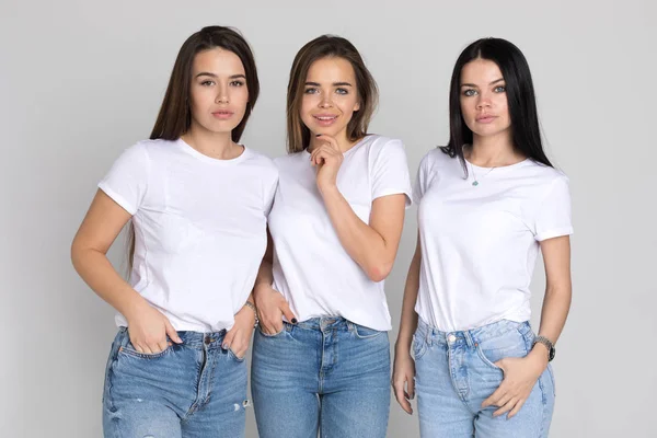 Tres hermosas y divertidas mujeres jóvenes en camisetas blancas y jeans sobre un fondo blanco . — Foto de Stock