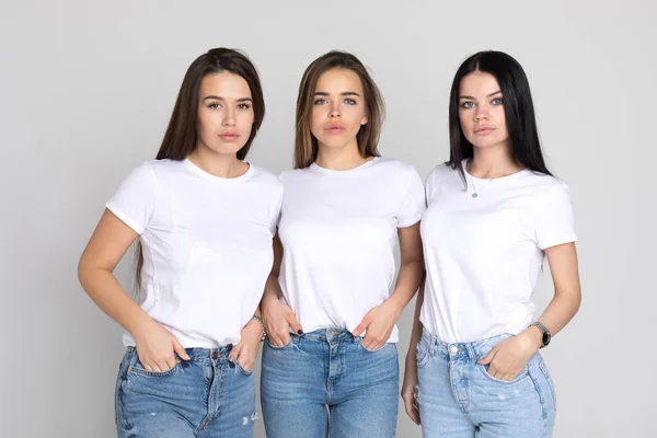 Три красивые и смешные молодые женщины в белых футболках и джинсах на белом фоне . — стоковое фото