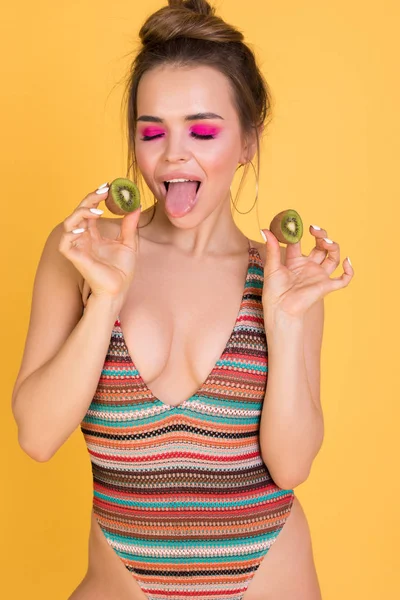 Girl in a swimsuit showing tongue and holding kiwi. — Stock Photo, Image