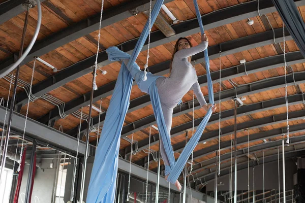 A beautiful gymnast girl is engaged in fly yoga on aerial canvases.