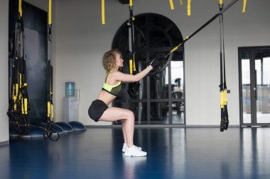 Spor salonunda yüzüklerle egzersiz yapan bir kadın..
