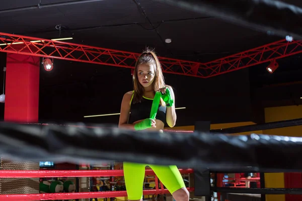 Atletisk flicka som står i ringen och rullar boxning bandage. Boxer flicka i neon leggings. — Stockfoto