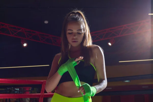 Atletisk flicka som står i ringen och rullar boxning bandage. Boxer flicka i neon leggings. — Stockfoto
