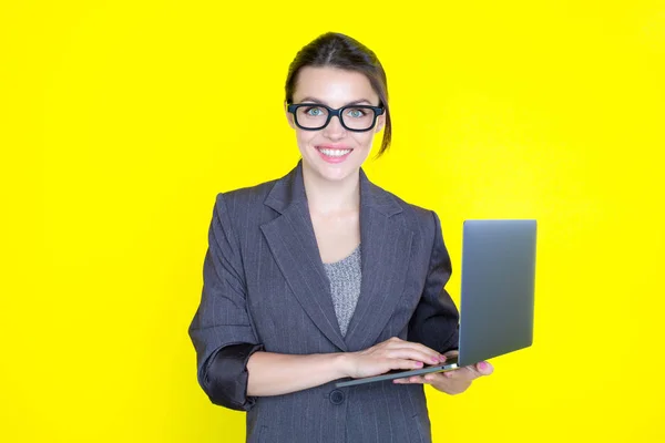 Business woman in suit with a laptop in hand on yellow background.