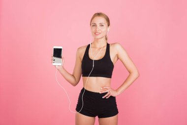 Kulaklıklı genç spor kadın telefonu kameraya gösteriyor.