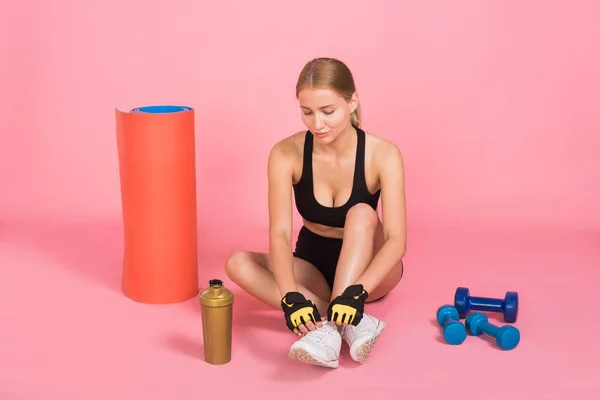 Genç sportif kadın pembe bir arka plan üzerinde oturuyor.