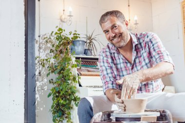 Bir erkek çömlekçi bir atölyede bir çömlek tekerleği üzerinde çalışır.