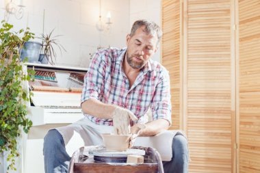 Bir erkek çömlekçi bir atölyede bir çömlek tekerleği üzerinde çalışır.