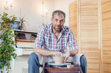 Bir erkek çömlekçi bir atölyede bir çömlek tekerleği üzerinde çalışır.