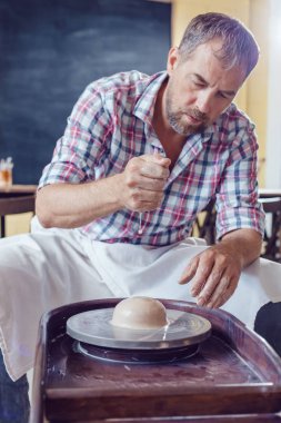 Bir erkek çömlekçi bir atölyede bir çömlek tekerleği üzerinde çalışır.