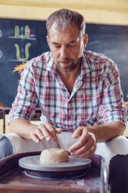 Bir erkek çömlekçi bir atölyede bir çömlek tekerleği üzerinde çalışır.