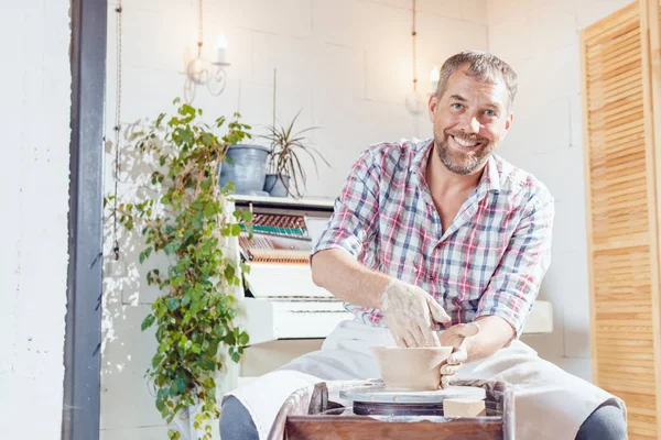 Bir erkek çömlekçi bir atölyede bir çömlek tekerleği üzerinde çalışır.