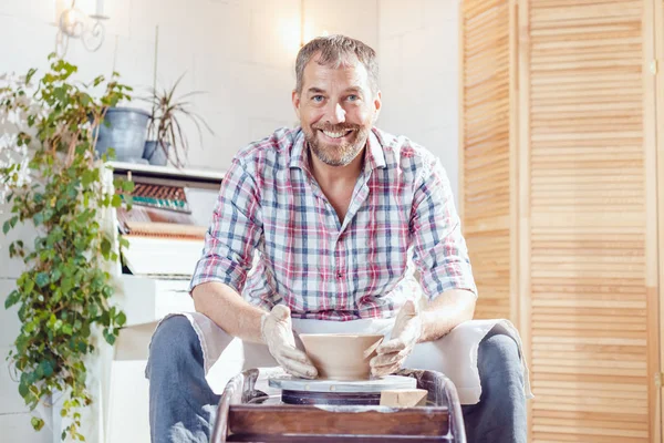 Bir erkek çömlekçi bir atölyede bir çömlek tekerleği üzerinde çalışır.