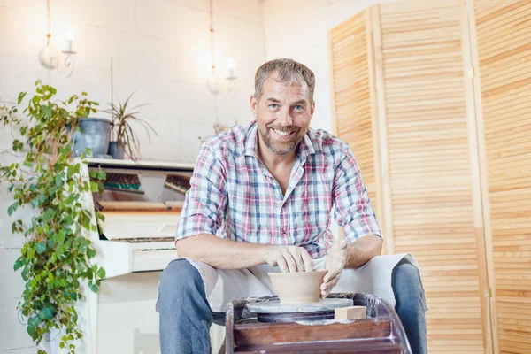 Bir erkek çömlekçi bir atölyede bir çömlek tekerleği üzerinde çalışır.