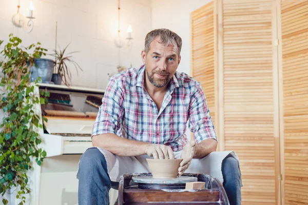 Bir erkek çömlekçi bir atölyede bir çömlek tekerleği üzerinde çalışır.