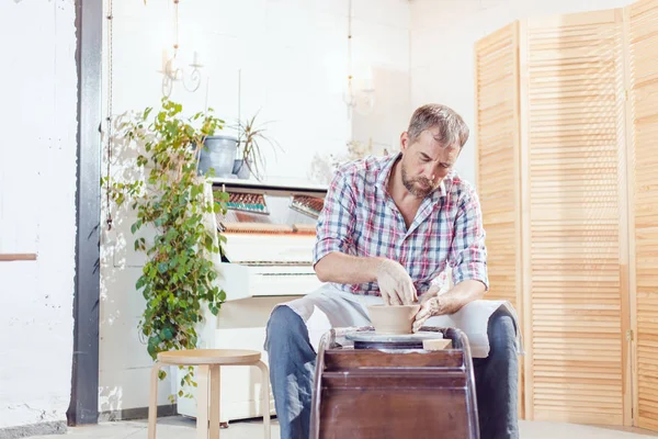 Bir erkek çömlekçi bir atölyede bir çömlek tekerleği üzerinde çalışır.