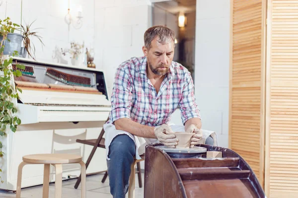 Bir erkek çömlekçi bir atölyede bir çömlek tekerleği üzerinde çalışır.