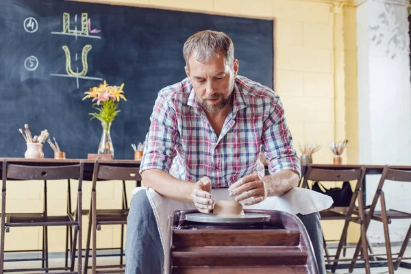 Bir erkek çömlekçi bir atölyede bir çömlek tekerleği üzerinde çalışır.