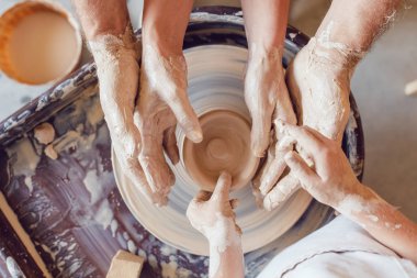 Potter 'ın elleri, çömlek tekeriyle çalışması için çocuğun ve kadının ellerine rehberlik ediyor..