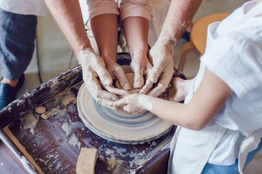 Potter 'ın elleri, çömlek tekeriyle çalışması için çocuğun ve kadının ellerine rehberlik ediyor..