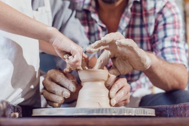 Potter 'ın elleri, çömlek tekeriyle çalışması için çocuğun ve kadının ellerine rehberlik ediyor..
