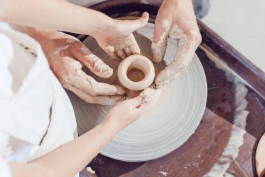 Potter 'ın elleri, çömlek tekeriyle çalışması için çocuğun ve kadının ellerine rehberlik ediyor..