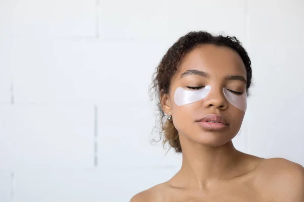 Jovem afro-americana com colágeno almofadas sob seus olhos no fundo branco . — Fotografia de Stock