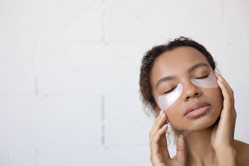 Young afro american woman with collagen pads under her eyes on white background.