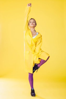 Sarı yağmurluk, mor tayt ve spor ayakkabı giyen genç bir kadın..