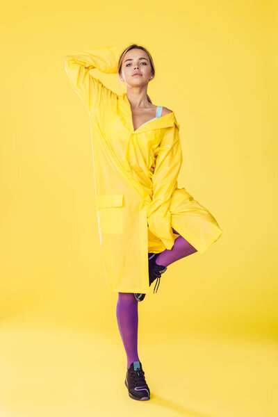 Young woman in a yellow raincoat, purple tights and sneakers.