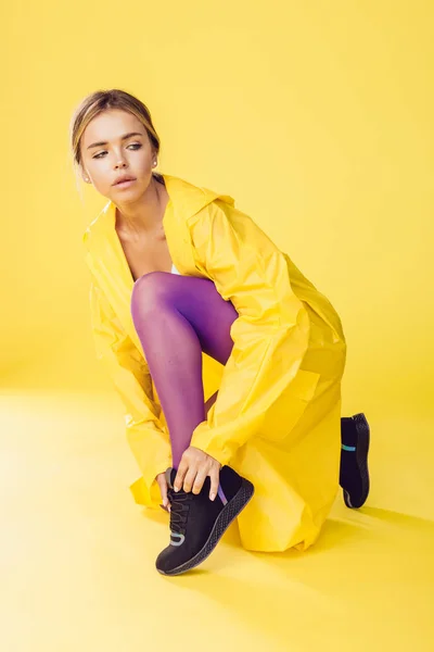 Молодая женщина в жёлтом плаще, фиолетовых колготках и кроссовках . — стоковое фото