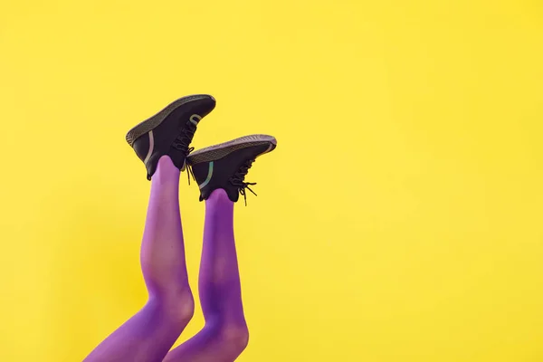Patas femeninas en medias y zapatillas púrpuras sobre un fondo amarillo . — Foto de Stock