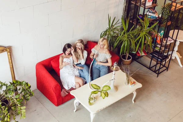 Trzy dziewczyny dziewczyny siedzą w kawiarni, rozmawiając i paląc hookah. — Zdjęcie stockowe