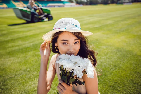 Portrait of a young asian woman in a hat. Woman holding a flower bouquet on nature background. — Stock Photo, Image