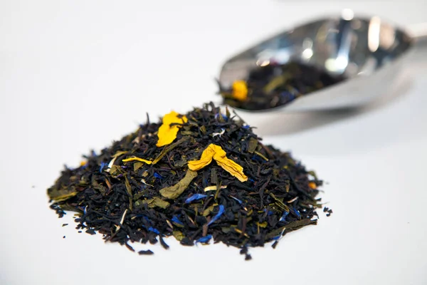 Uma colher de metal com folhas de chá secas fica ao lado de um monte de folhas de chá — Fotografia de Stock