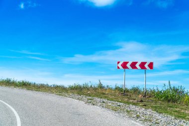 Uyarı işareti keskin, mavi gökyüzü, iyi bir yol açmak. Dağlarda tehlikeli yol.