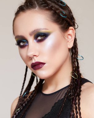 Parlak, yaratıcı makyajlı ve kafasında örgüler olan genç bir kız. Amazon suretinde parlayan derisi ve burnunda küpesi olan güzel bir manken. Güzel surat..